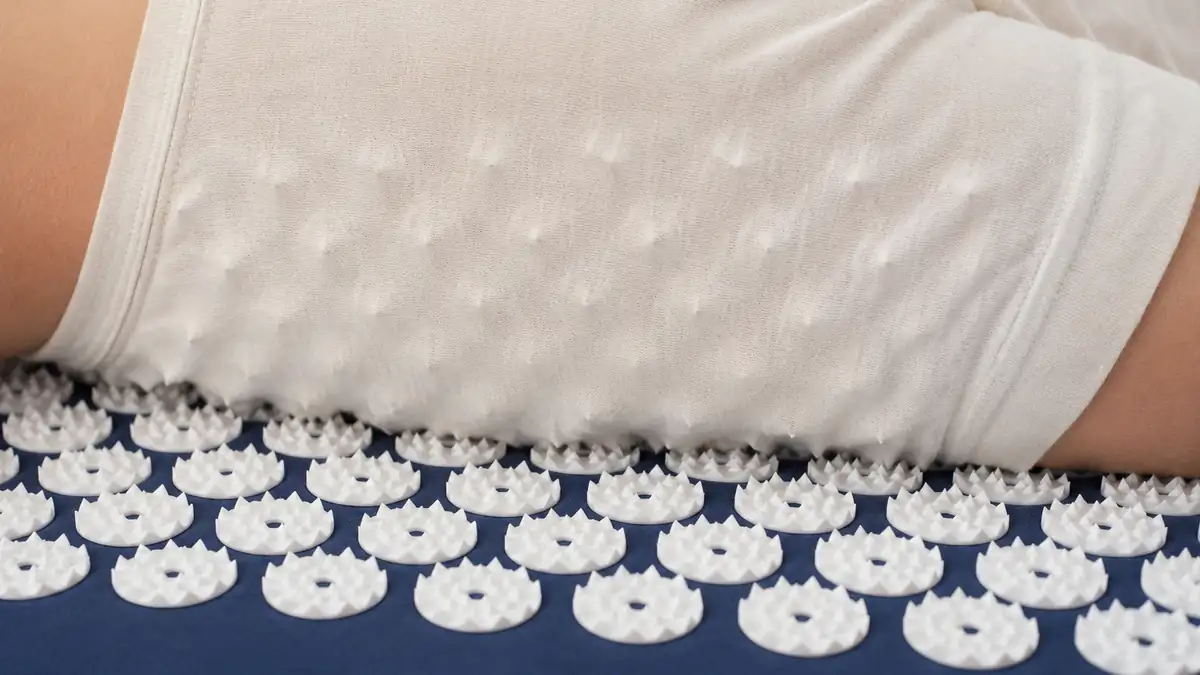 Upper back resting on the white spikes of a navy acupressure mat through a thin shirt