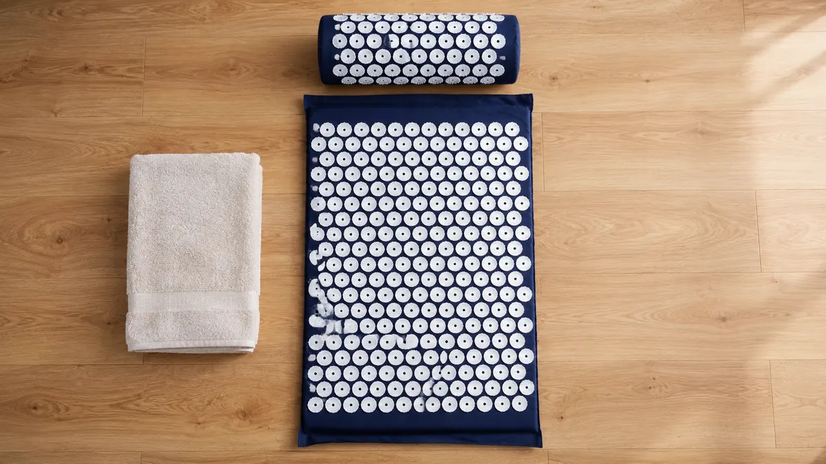 Navy acupressure mat and bolster pillow laid out ready on a wooden floor with a folded towel