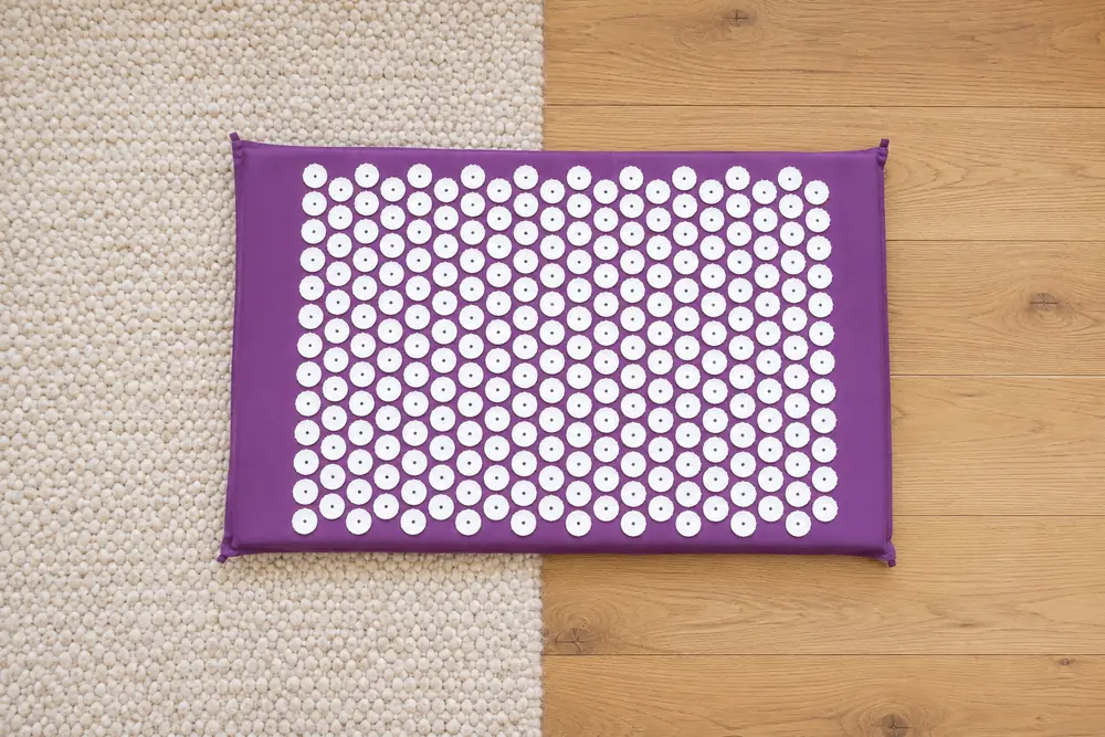 Purple SpikeRest mat placed half on a wool rug and half on bare wooden floor, seen from above