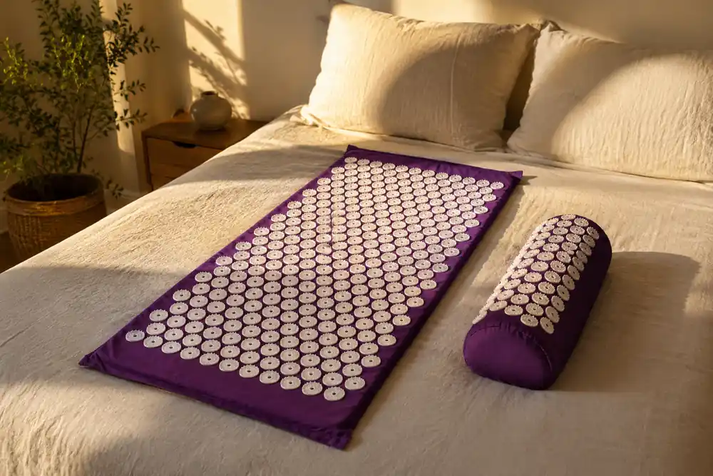 Purple SpikeRest acupressure mat and bolster pillow laid across a made bed in late afternoon light