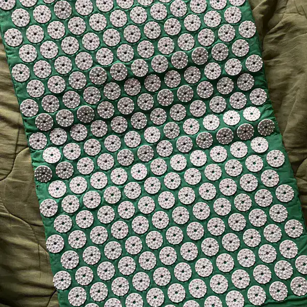 SpikeRest acupressure mat in Green unrolled on a bed