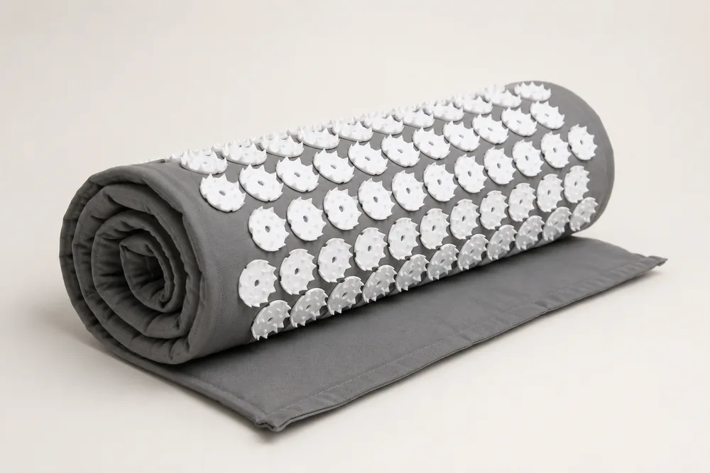 A gray SpikeRest acupressure mat loosely rolled up on a plain surface, spikes visible along the roll